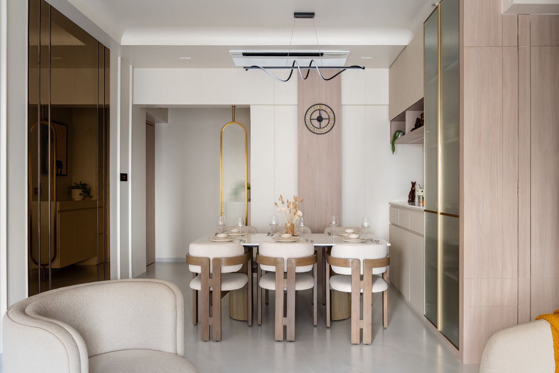 The dining area, framed by tinted bronze-glass and fluted-glass cabinetry, with a sculptural ribbon pendant suspended over a marble-topped table