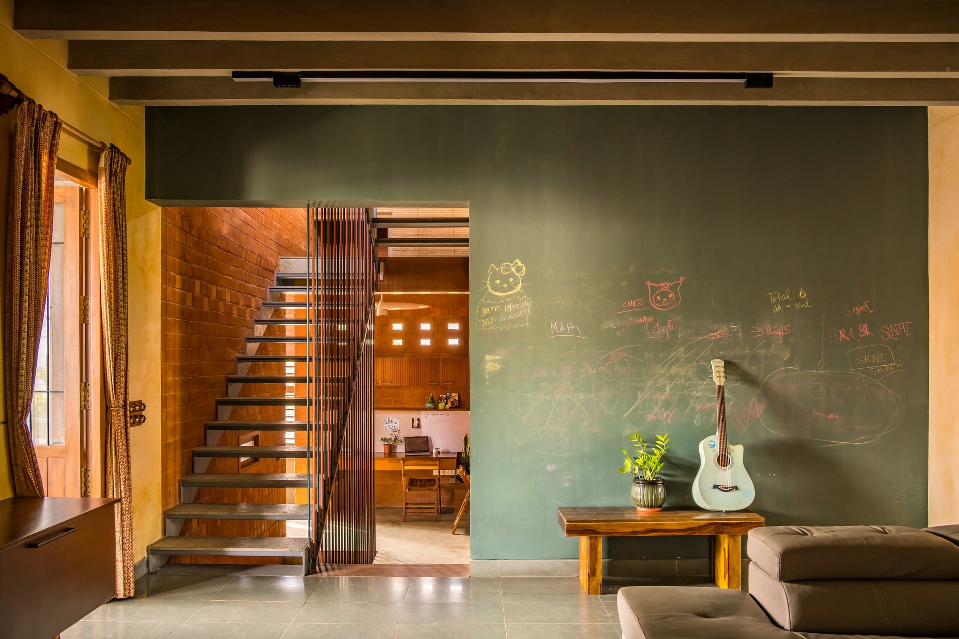 A chalkboard wall and steel-stringer staircase mark the transition between family room and study