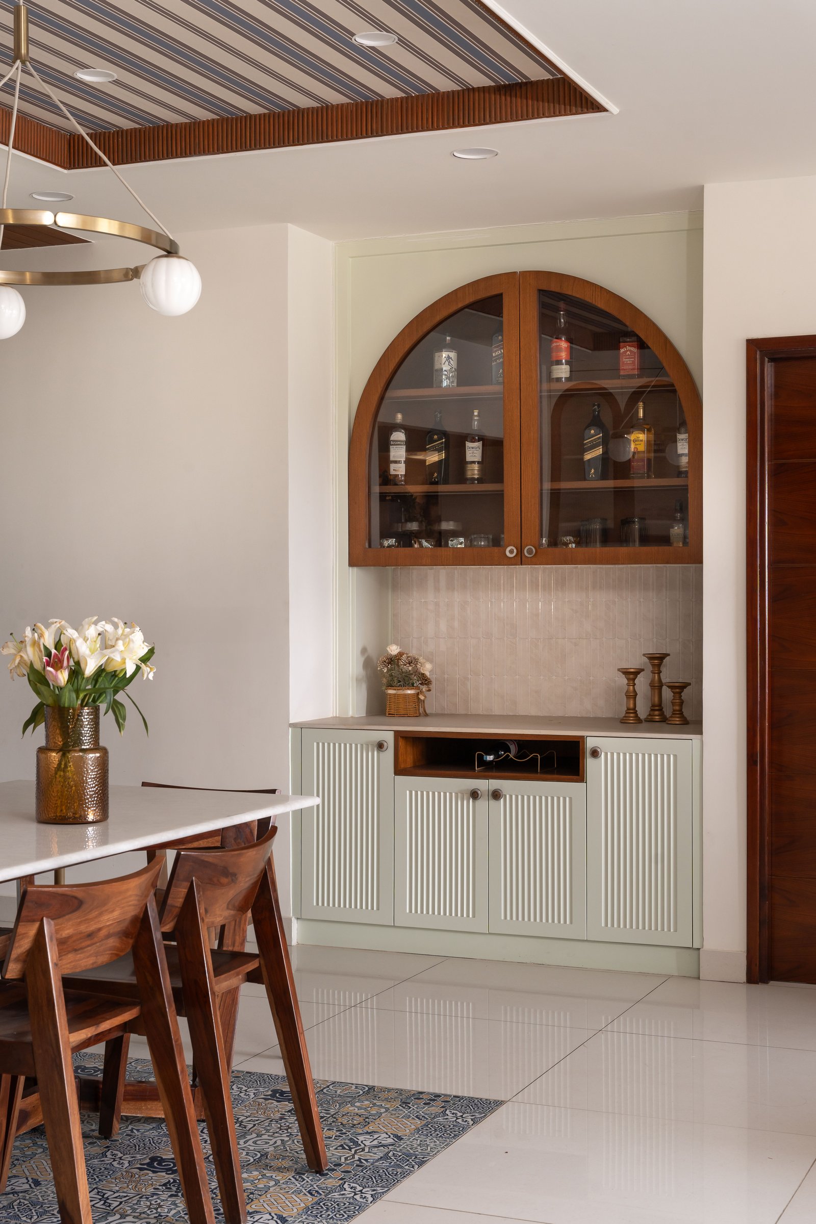The bar niche in muted sage green, with fluted lower shutters and an arched glass upper cabinet