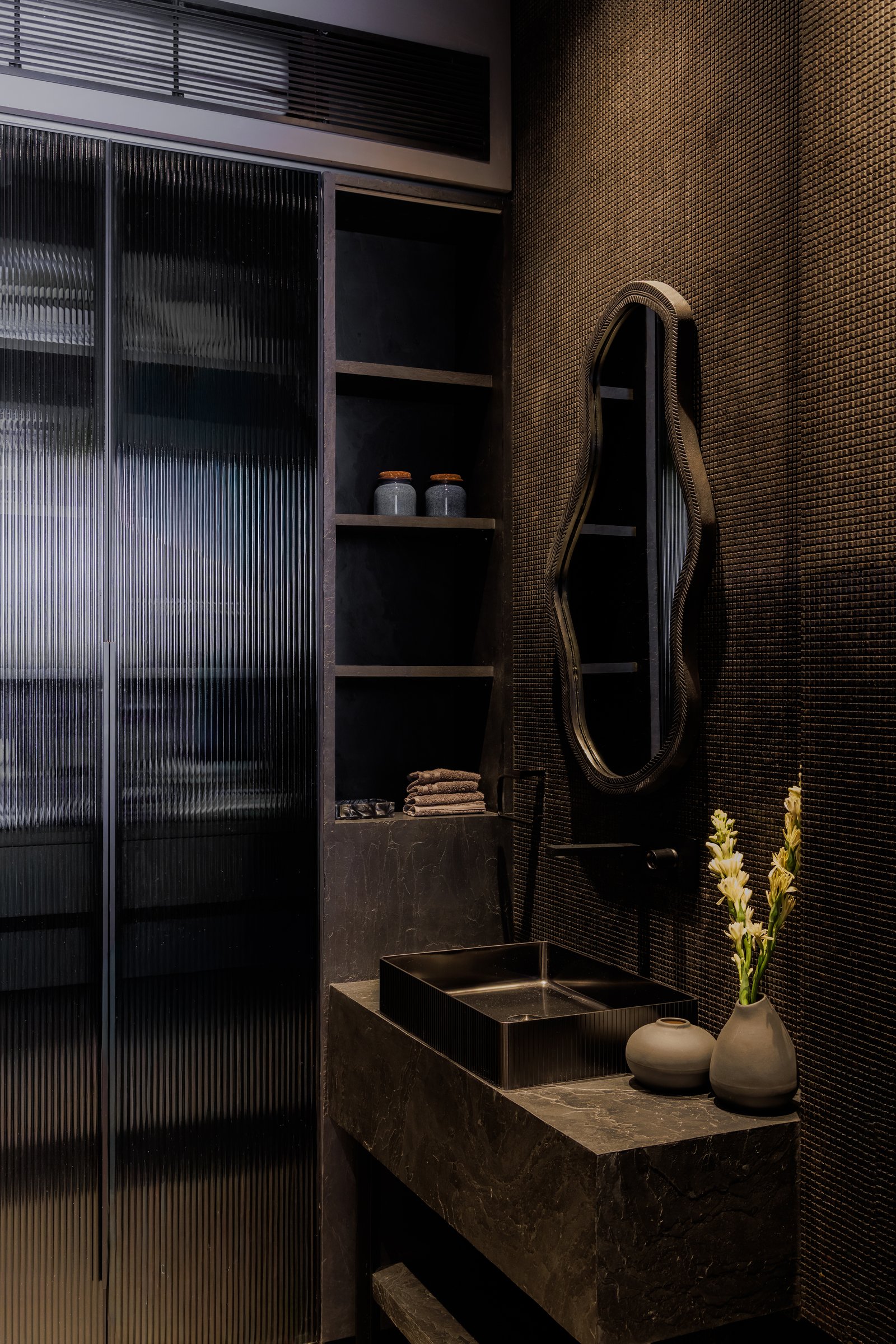 The powder room, where a textured woven wall covering in deep bronze wraps a dark stone vanity and a hand-worked wall mirror