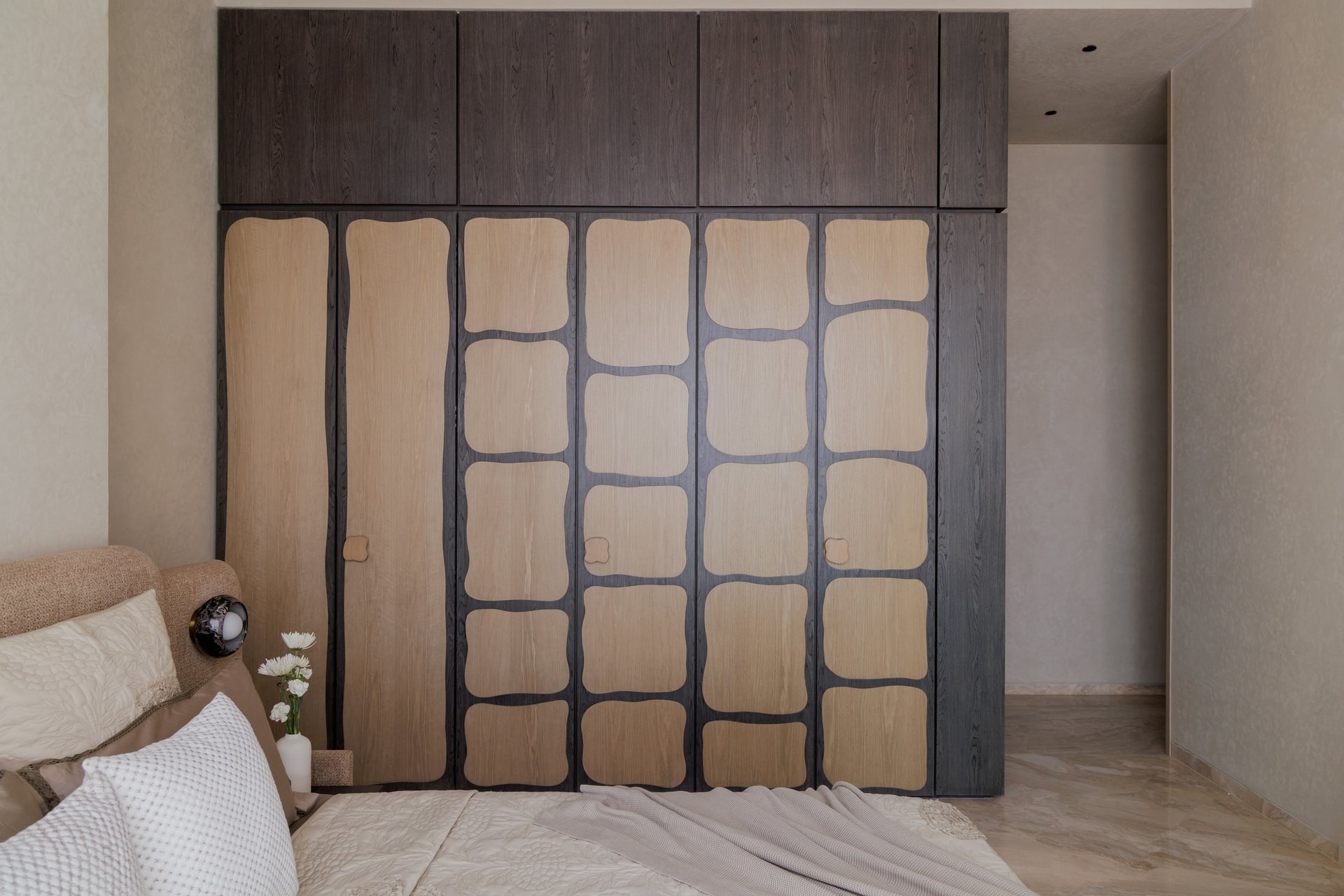 A wall of wardrobes in the guest bedroom, where pale oak panels are inlaid into a darker grid in rounded, organic rectangles