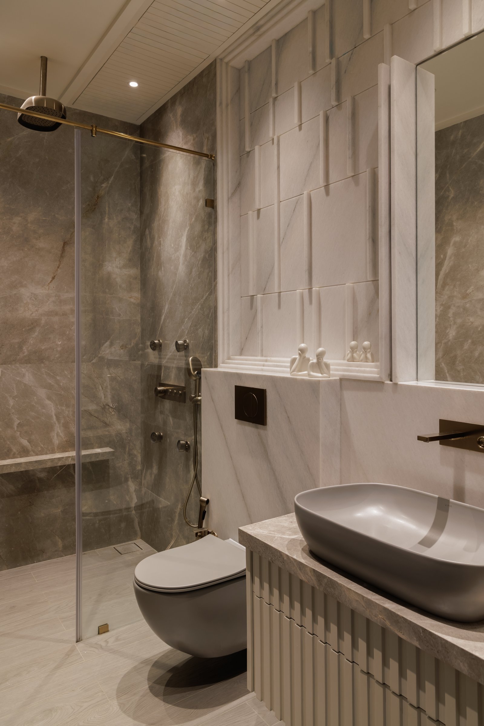 The primary bathroom, where veined grey stone meets a pale marble wall carrying a raised composition of overlapping panels