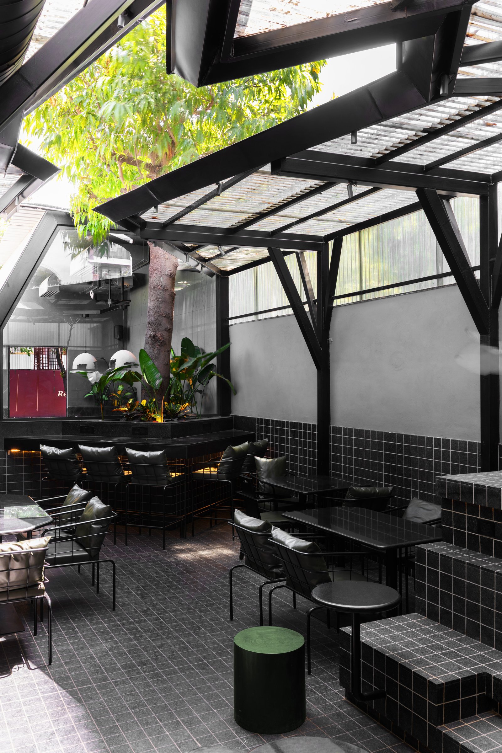 The main seating volume, framed by a pitched steel roof and centred on the tree