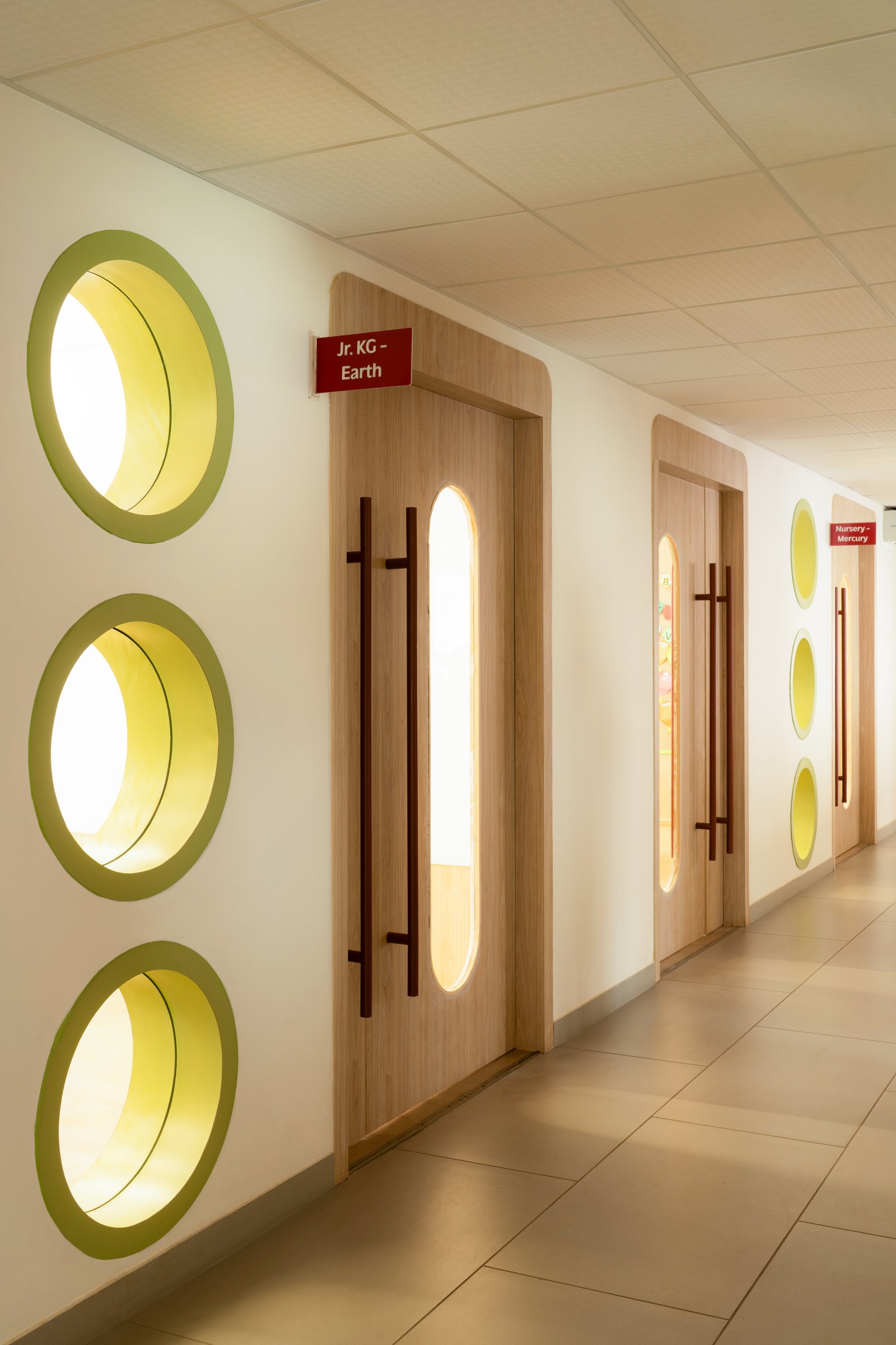 A closer view of the corridor wall, where three stacked circular apertures glow between capsule-cutout doors