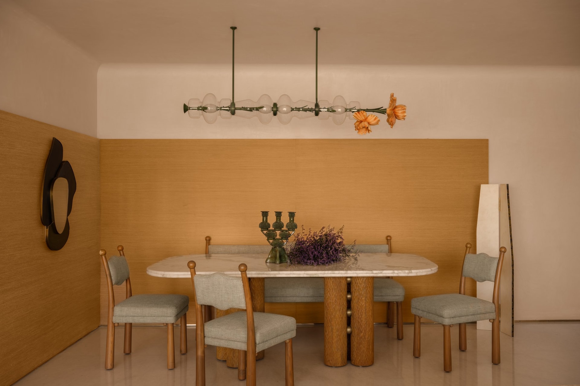 The dining area, where a suspended glass-and-floral installation hovers over a marble-topped table anchored by a ribbed wooden base