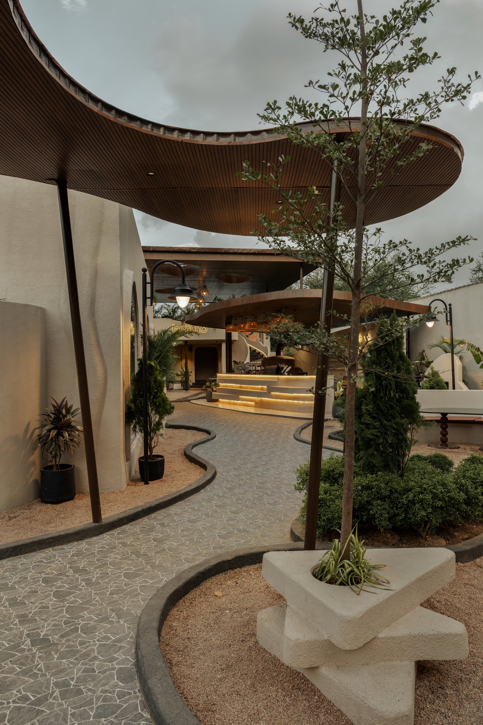 Overlapping curved canopies hover above meandering stone pathways and gravel beds, treating landscape as continuous architecture
