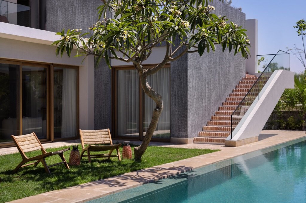 A textured grey facade meets the lap pool, with terracotta stairs and a frangipani in bloom softening the composition.