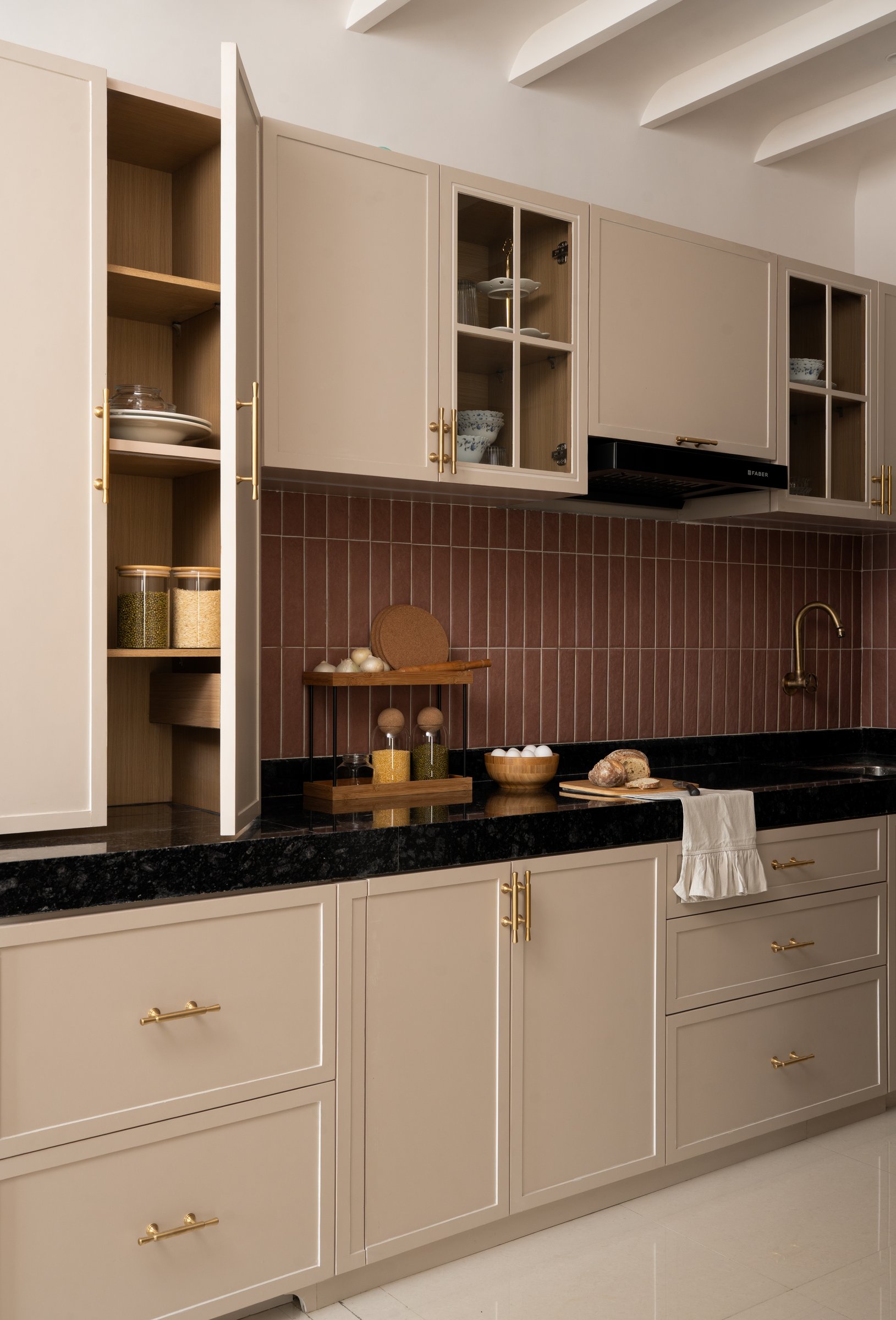 The kitchen, where muted cabinetry meets a rust-toned tile backsplash beneath a fluted ceiling