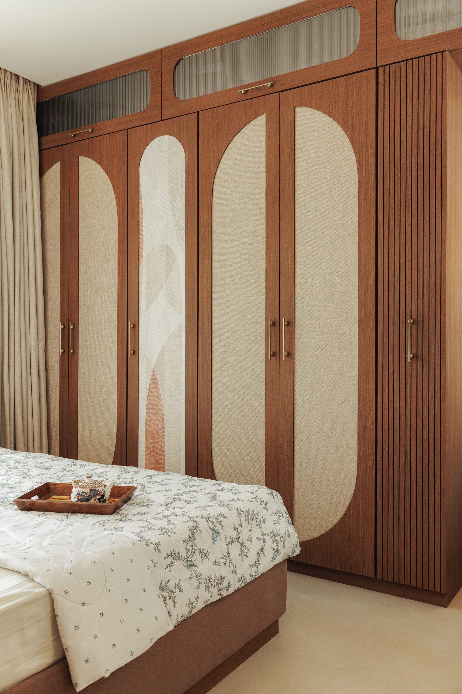 The wardrobe wall in warm timber, inset with oatmeal fabric panels and a graphic curved motif