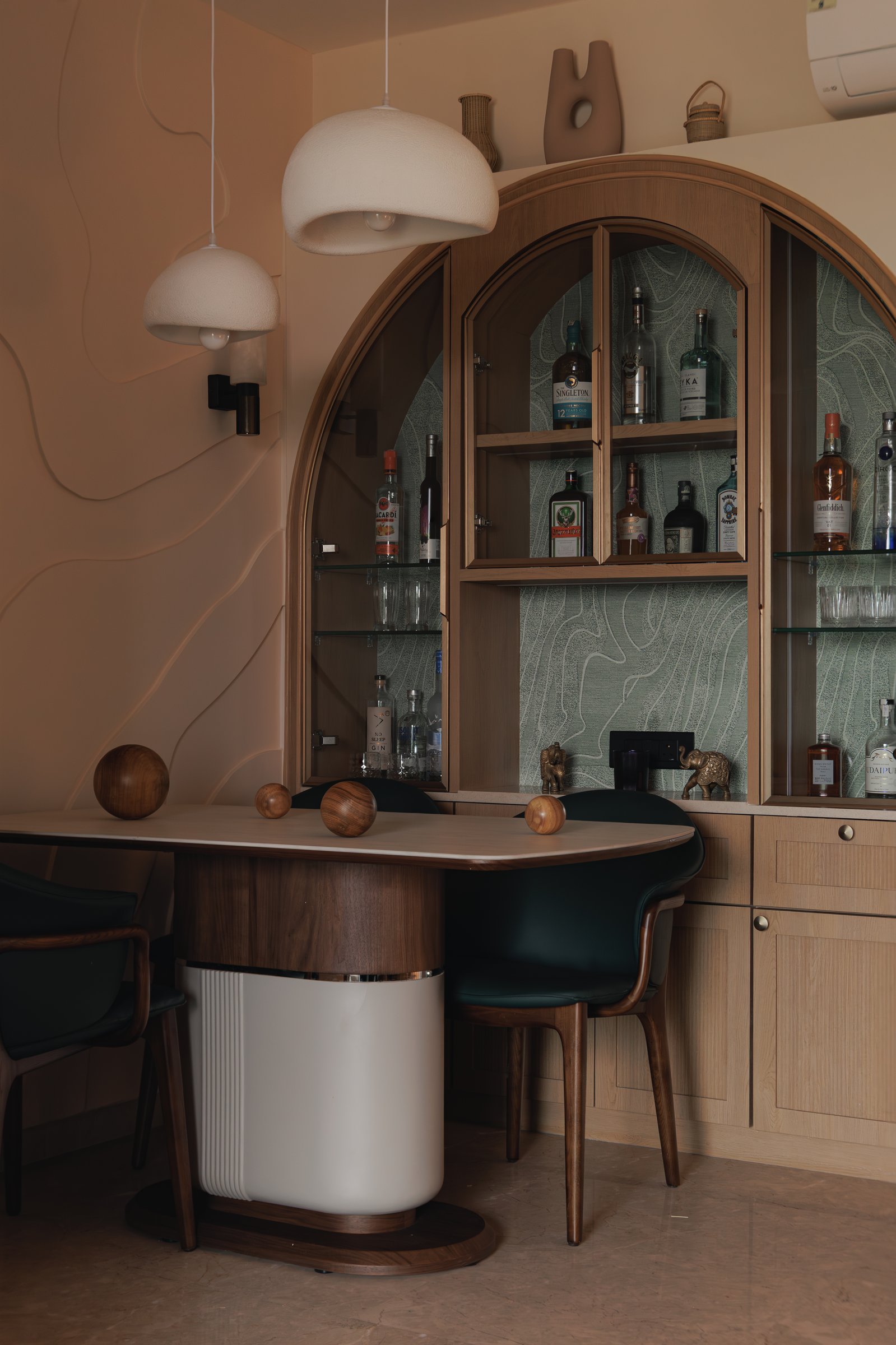 The arched bar cabinet in warm oak, lined with green topographic wallpaper