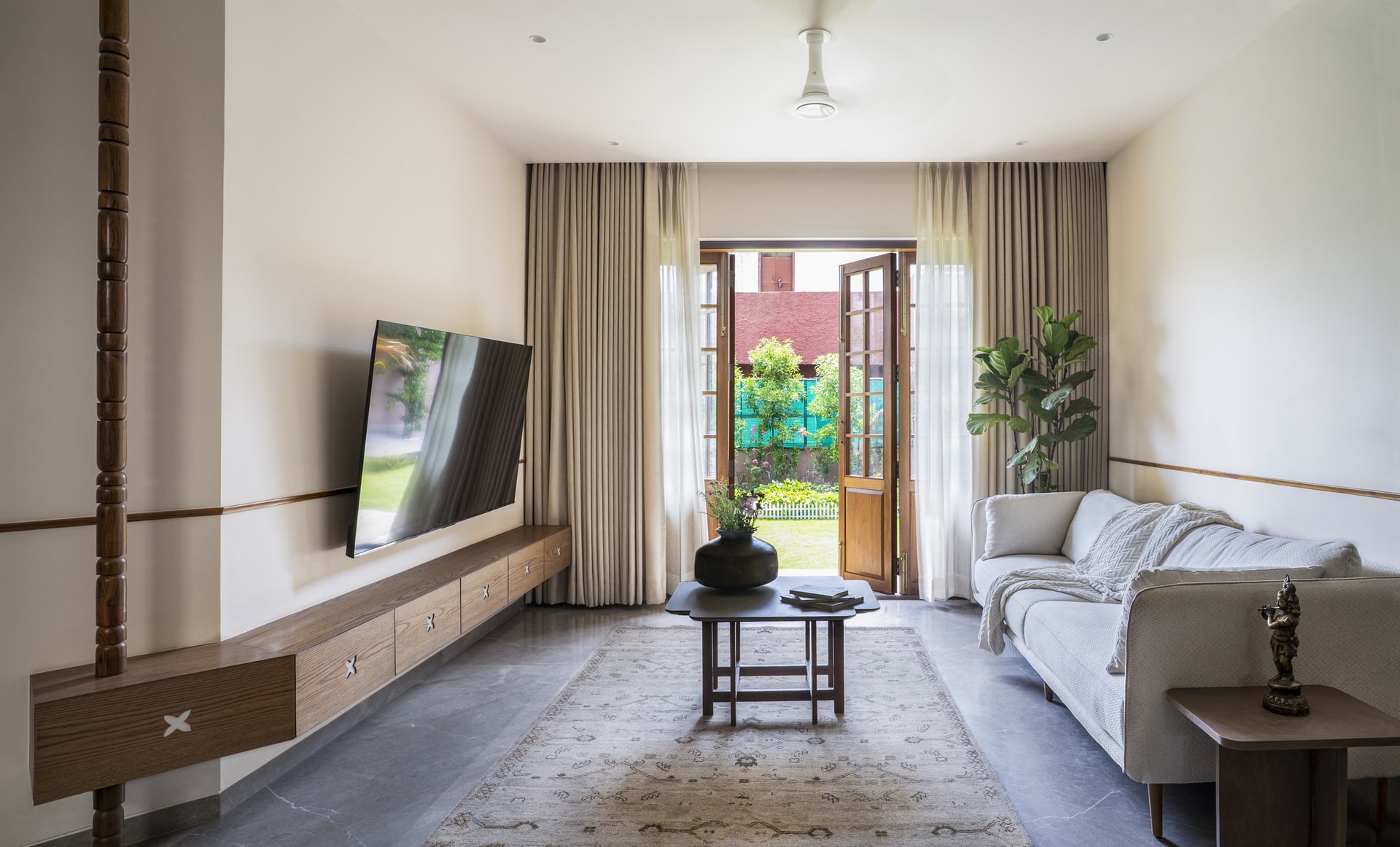 The living room opens to the garden through timber-framed glazed doors, with a low media unit inlaid with small mother-of-pearl detailing