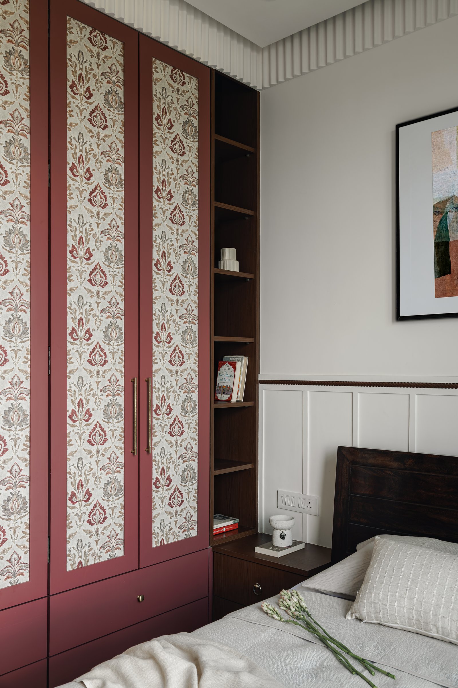 A wider view of the wardrobe wall, with an open shelving column in dark wood set between the rose-finish units