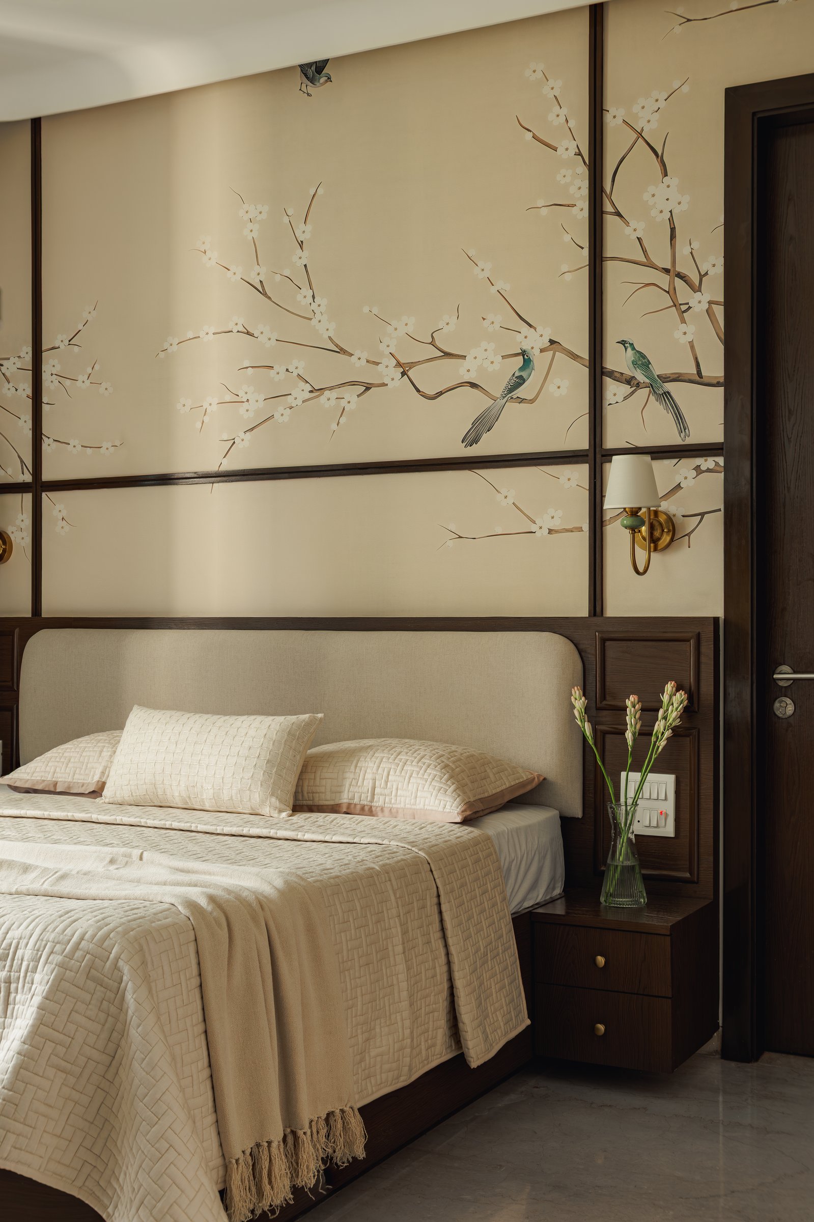 The primary bedroom, where a botanical wallpaper framed in dark wood panelling defines the headboard wall