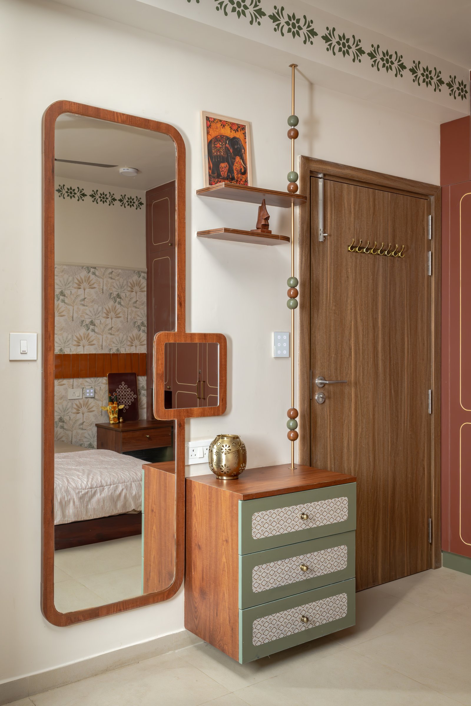 A dressing area with a full-length wooden-framed mirror beside a floating chest in sage with patterned inserts